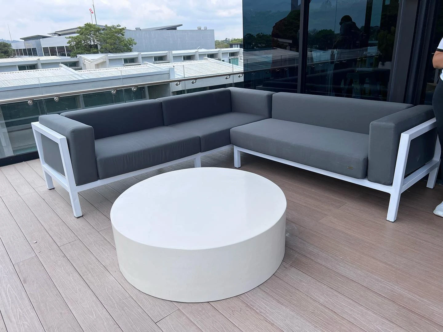 Mesa de centro redonda de concreto blanco sobre un deck de madera, frente a un sofá gris de exterior