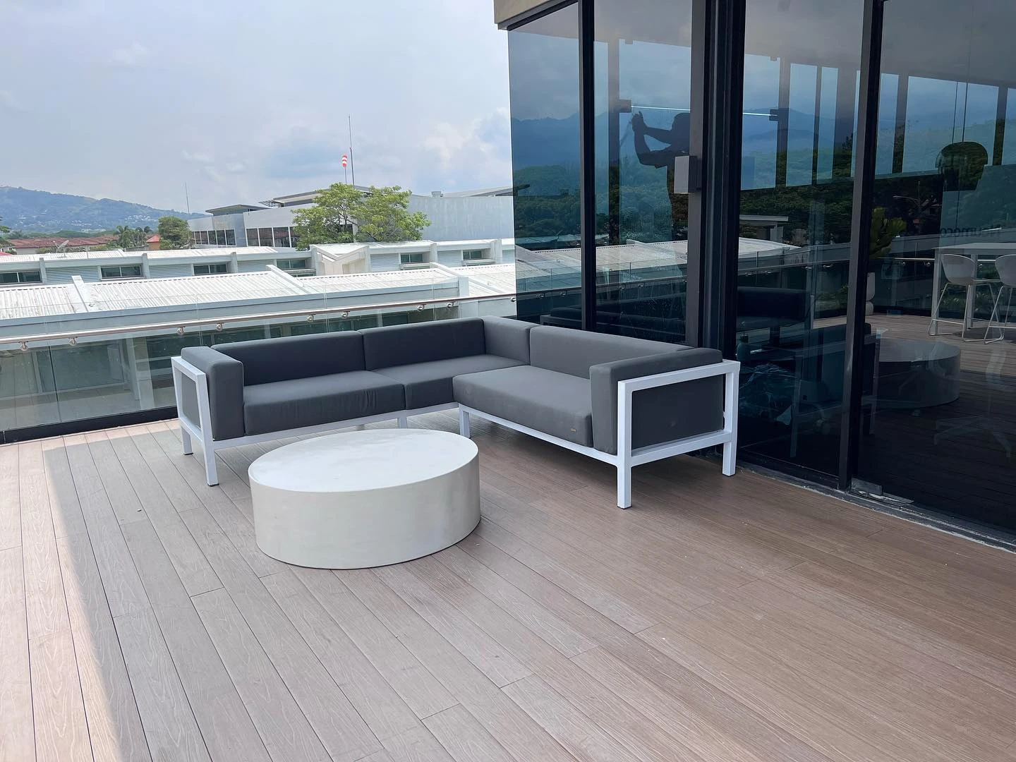 Mesa de centro redonda de concreto blanco sobre un deck de madera, frente a un sofá gris de exterior. Vista adicional 1.