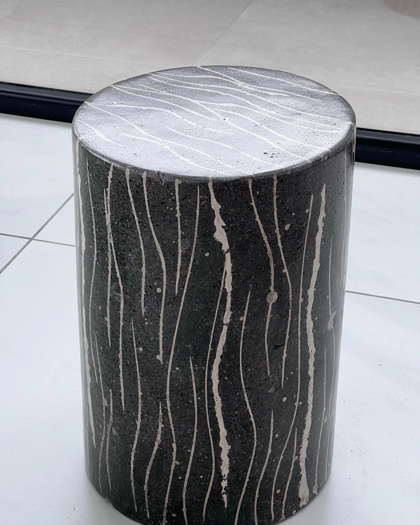 Mesa auxiliar cilíndrica de concreto negro con vetas blancas verticales