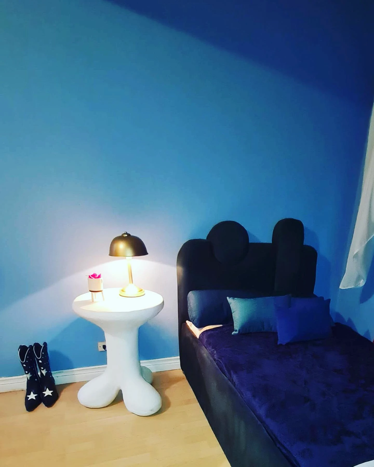Mesa pedestal blanca de concreto con una lámpara dorada encima, en una habitación de paredes azul intenso