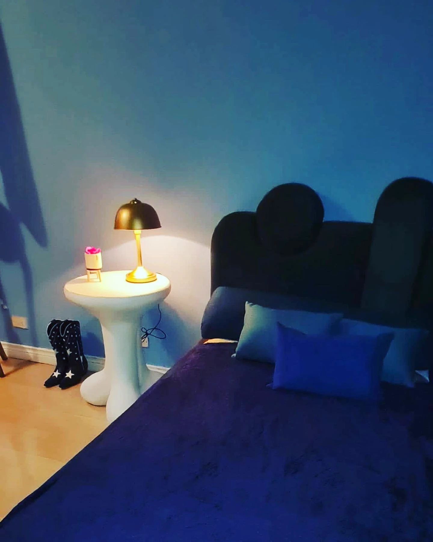 Mesa pedestal blanca de concreto con una lámpara dorada encima, en una habitación de paredes azul intenso. Vista adicional 1.