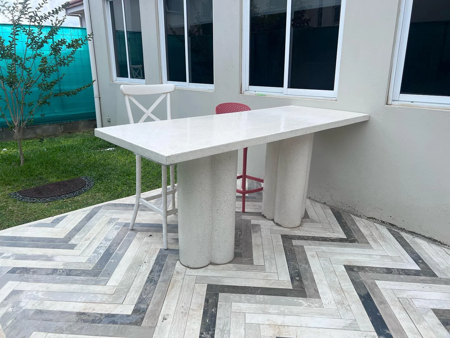 Mesa alta de terrazo blanco sobre base de columnas, en una terraza con piso de espiga en blanco y gris