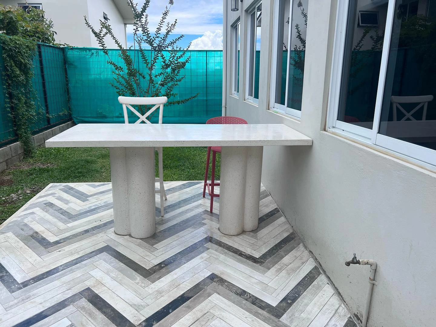 Mesa alta de terrazo blanco sobre base de columnas, en una terraza con piso de espiga en blanco y gris. Vista adicional 1.