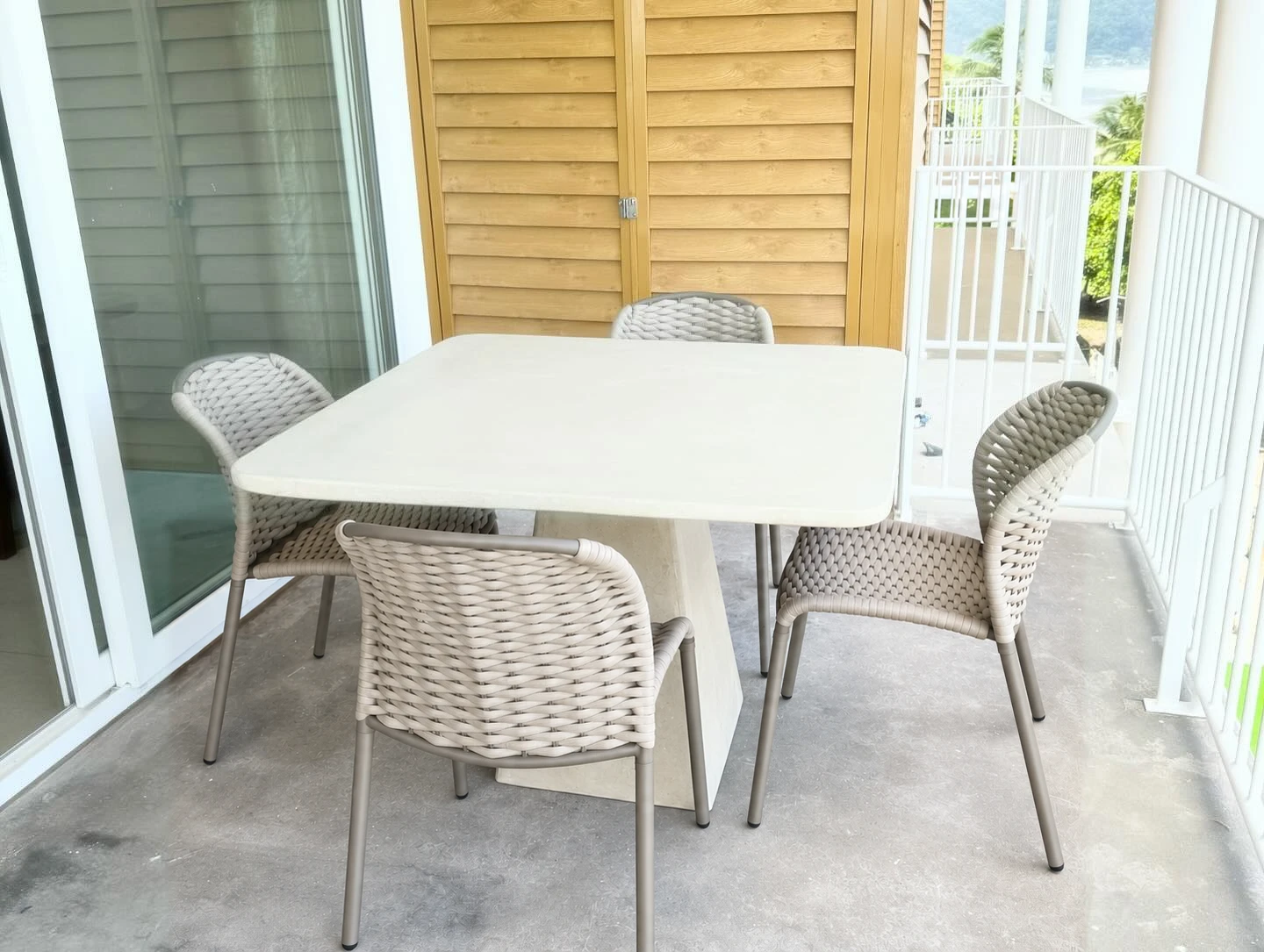 Mesa ovalada de terrazo blanco con agregado oscuro, rodeada de sillas rosadas y verdes en una terraza. Vista adicional 1.