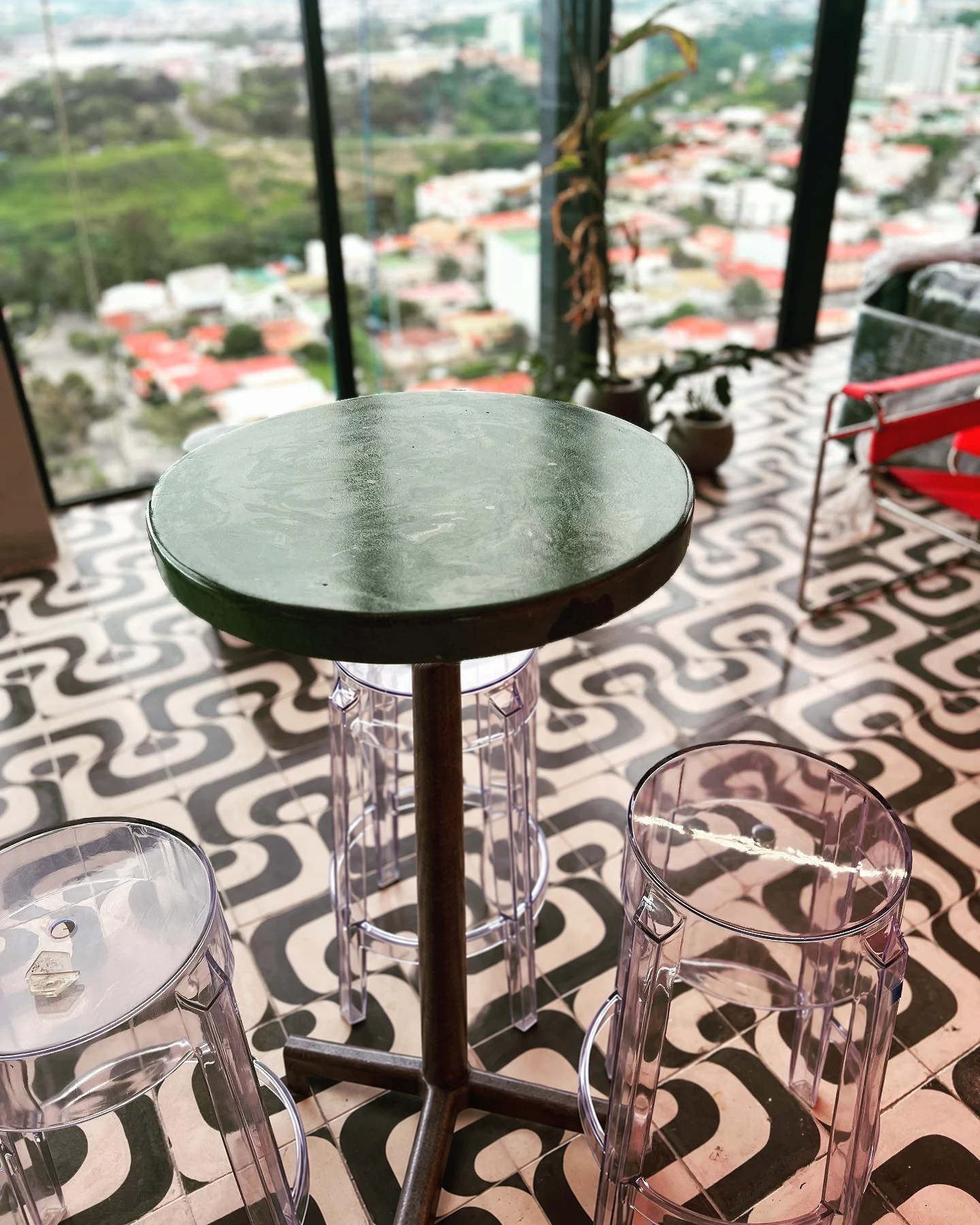 Mesa redonda de concreto verde marmoleado sobre un piso de mosaico gráfico en blanco y negro, junto a un ventanal