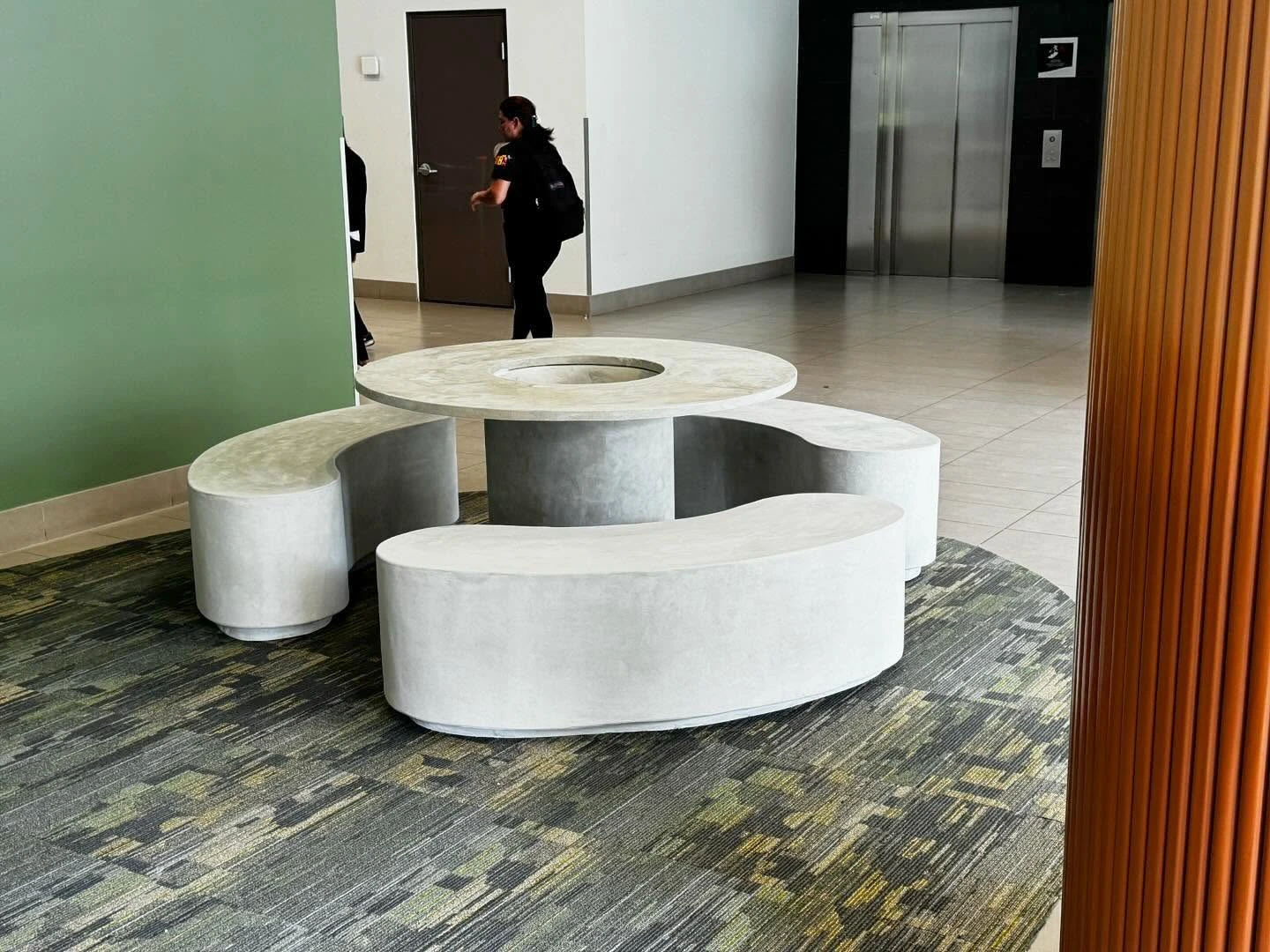 Mesa redonda de concreto gris con dos bancas curvas alrededor, en el vestíbulo de un edificio corporativo
