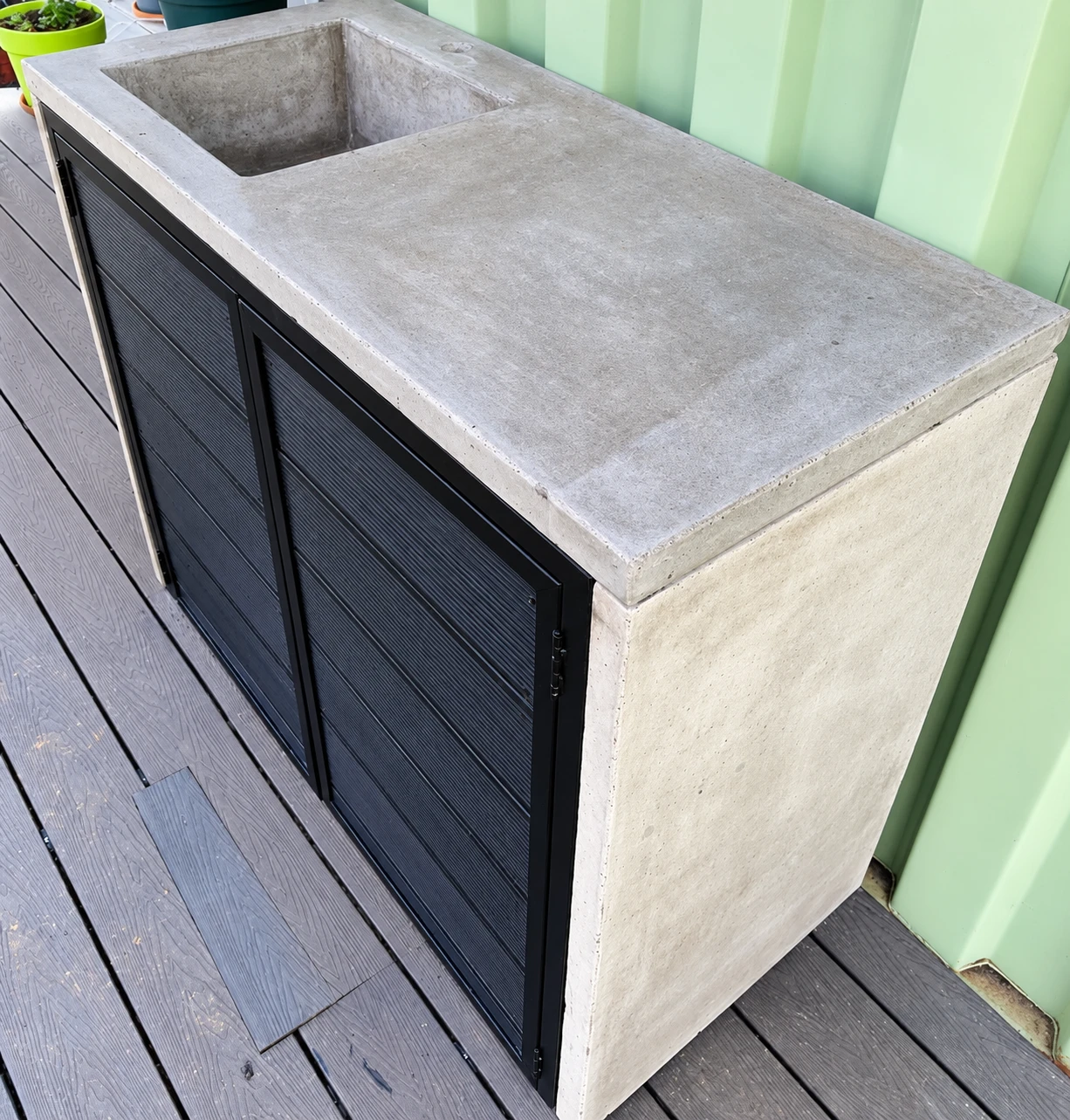 Pila de concreto claro con poza y escurridero montada sobre un mueble de madera oscura, en una terraza de deck