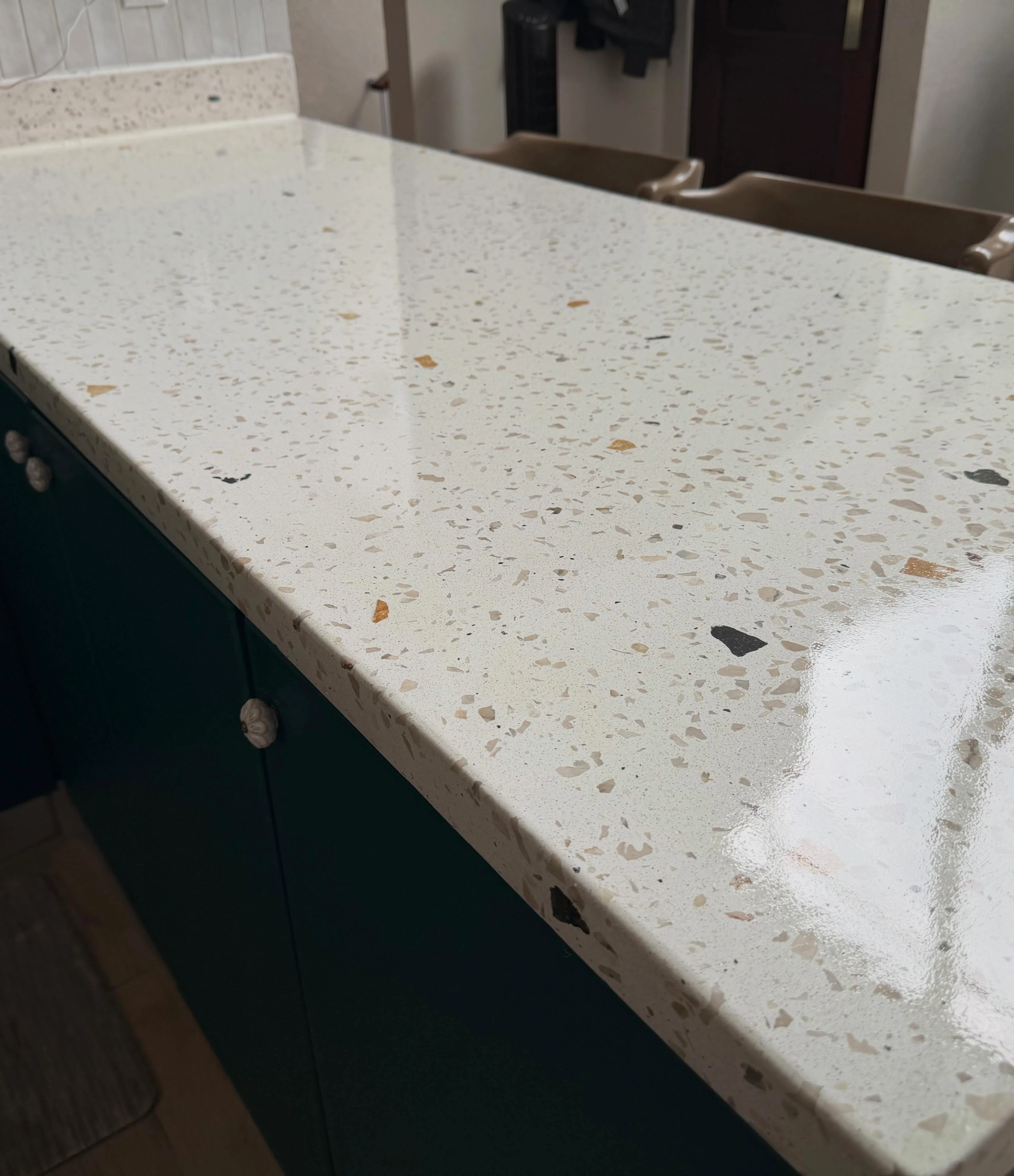 Sobre de terrazo blanco con agregado fino sobre un mueble verde oscuro, con grifería de pared