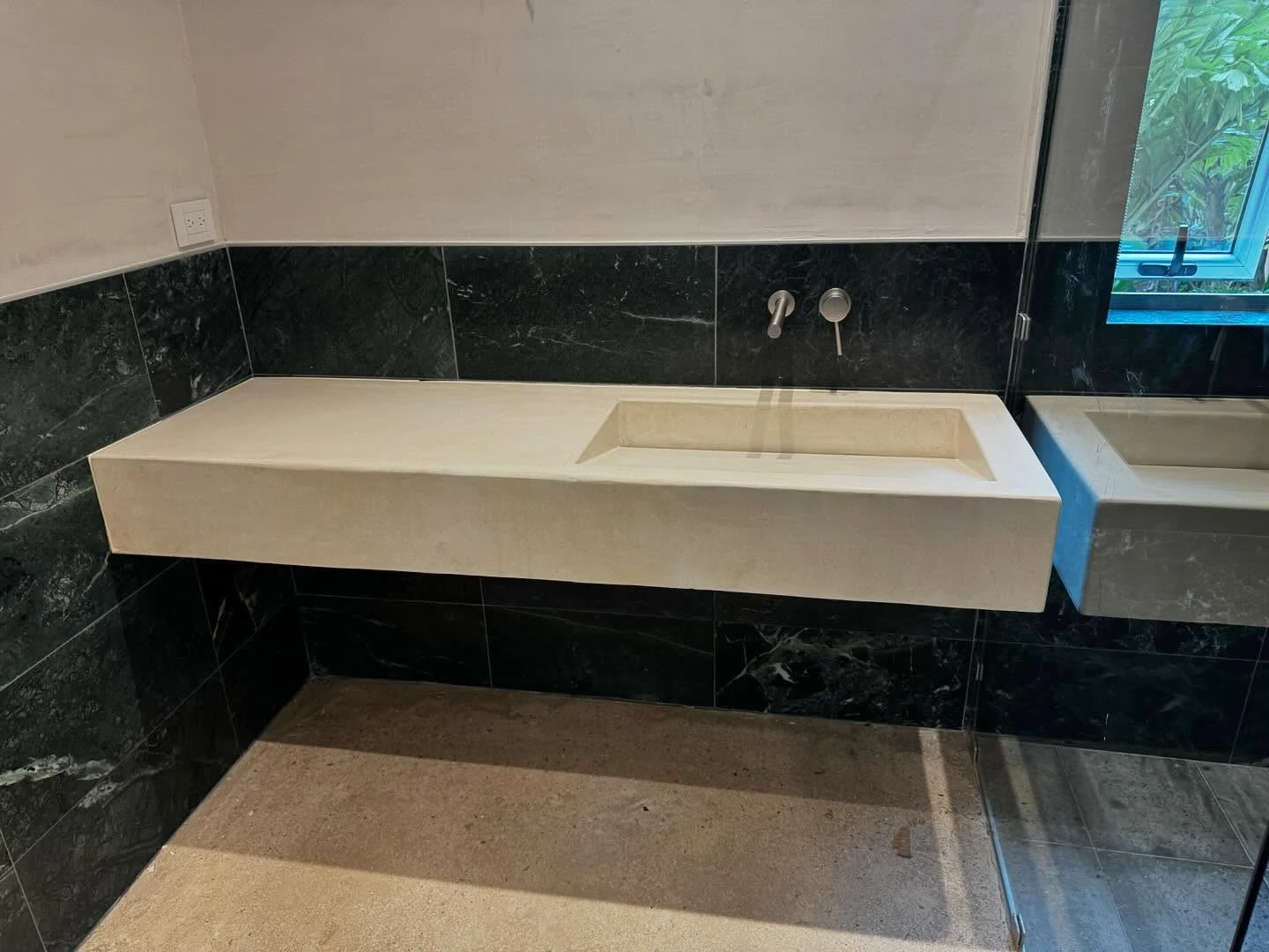 Sobre volado de concreto blanco con poza rectangular integrada, contra pared de mármol verde oscuro