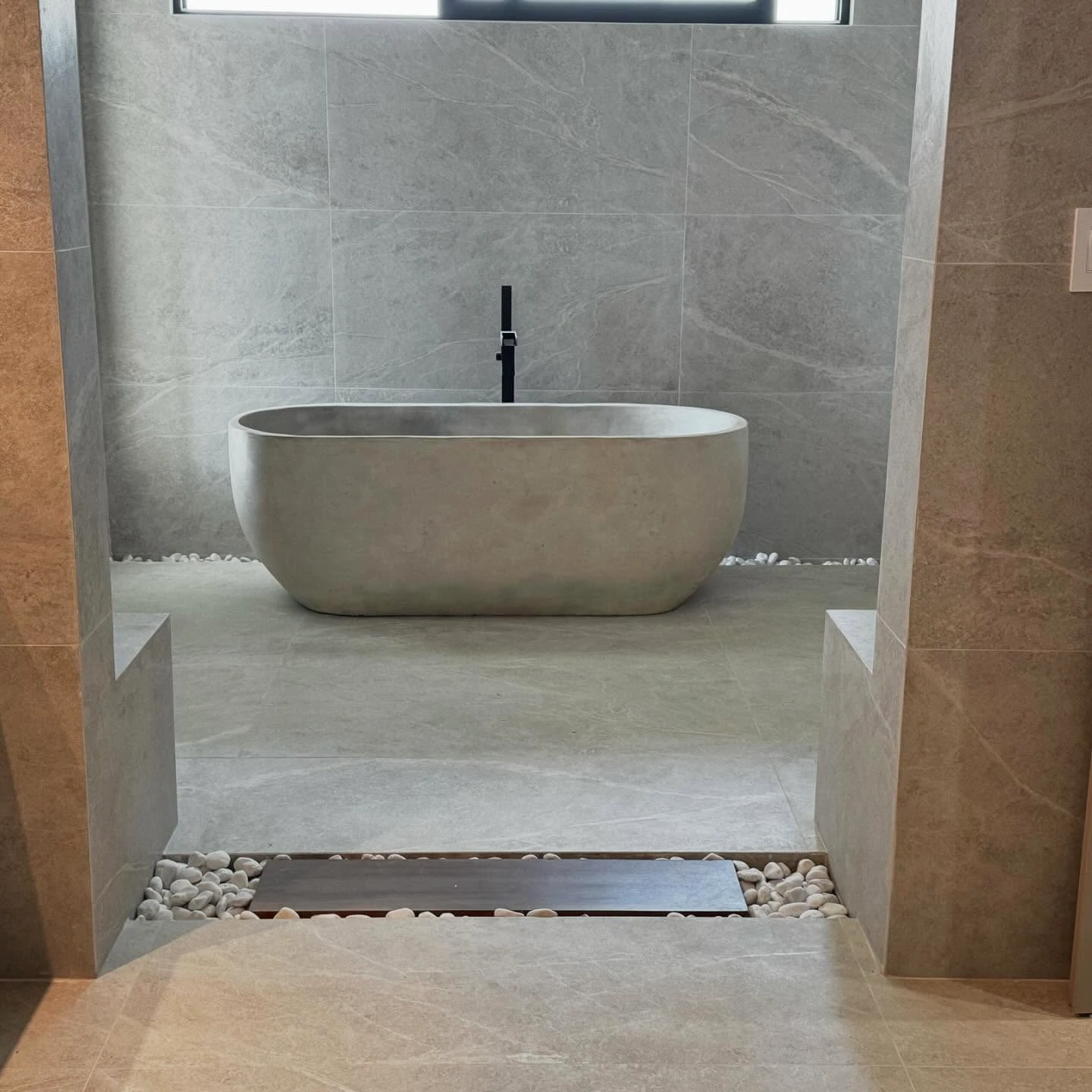 Tina ovalada de concreto gris con canto ancho, en un baño con paredes de porcelanato gris